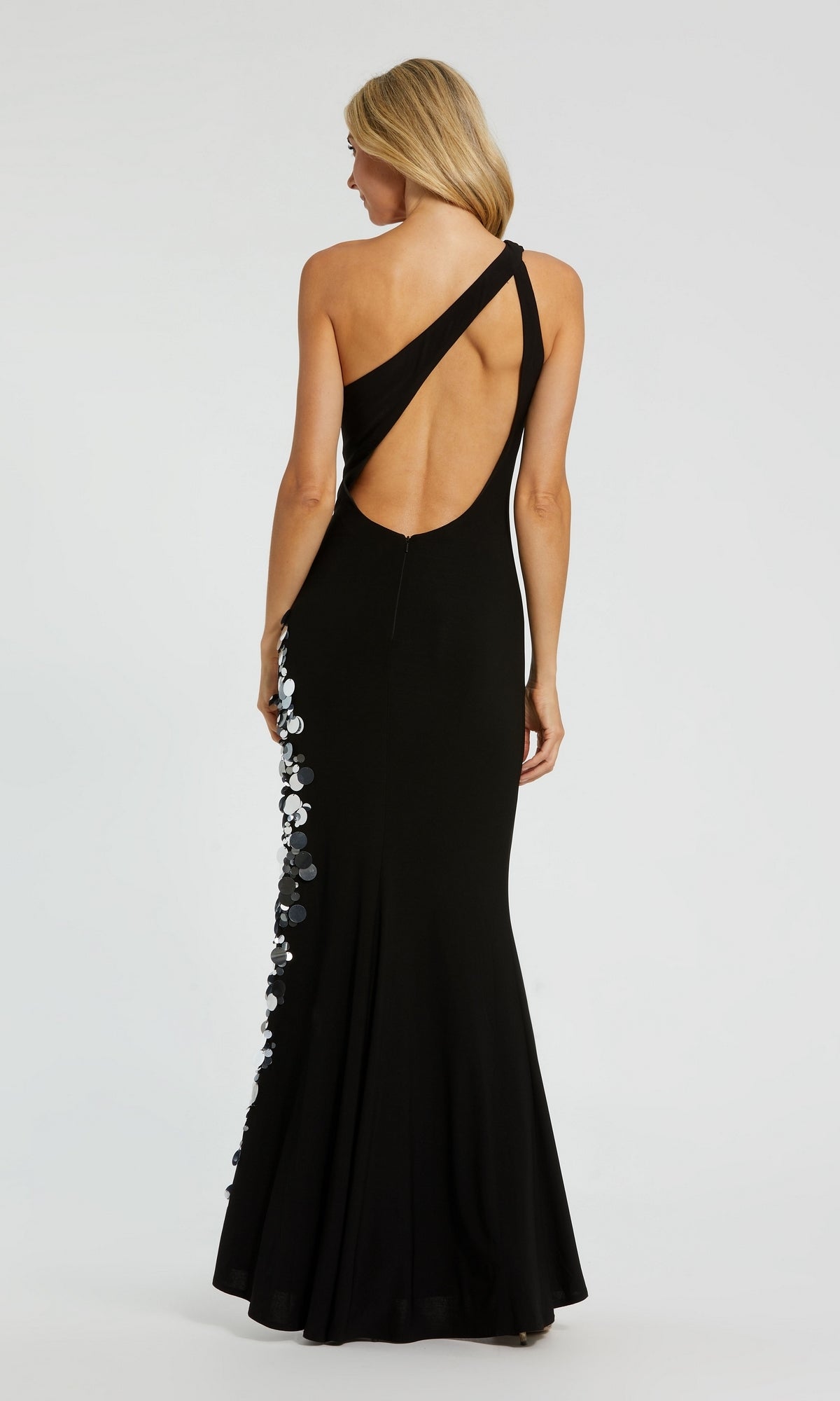 Woman wearing the Mac Duggal Long Formal Dress 44037—black, fitted, one-shoulder with an open back and sequin side embellishments—stands against a plain background.